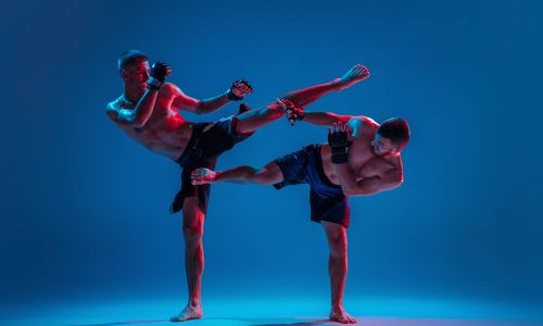 Tensioned. MMA. Two professional fighters punching or boxing isolated on blue studio background in neon. Fit muscular caucasian athletes or boxers fighting. Sport, competition and human emotions, ad.